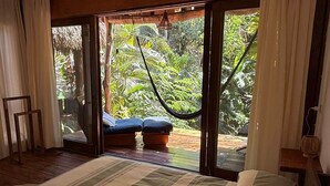 A bedroom with a large bed, a hammock, and a view of lush greenery outside. - AC Room with Balcony and Nature Views (Santa María Tonameca)