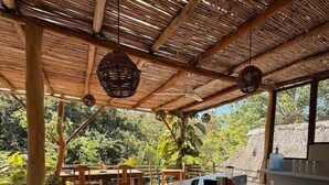 A covered outdoor area with a long table, chairs, and a kitchen counter with various items. - AC Room with Balcony and Nature Views (Santa María Tonameca)