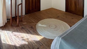 A room with wooden flooring, two wooden doors, a ceiling fan, an air conditioning unit, and a round rug. - AC Room with Balcony and Nature Views (Santa María Tonameca)