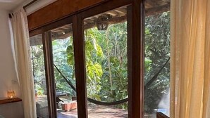 A room with a large sliding glass door leading to an outdoor deck with a hammock and lush greenery. - AC Room with Balcony and Nature Views (Santa María Tonameca)