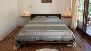 A bedroom with a bed, wooden floor, ceiling fan, bedside lamps, and a window with curtains. - AC Room with Balcony and Nature Views (Santa María Tonameca)