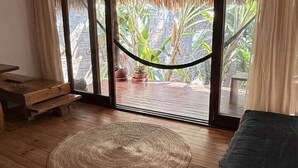 A room with a wooden floor, a woven rug, a hammock, and a view of a garden through large glass doors. - Loft with Balcony and Nature Views (Santa María Tonameca)