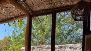 A room with a thatched roof, a window with a view of trees, a water dispenser, and a shelf with glasses and a decorative pot. - Loft with Balcony and Nature Views (Santa María Tonameca)
