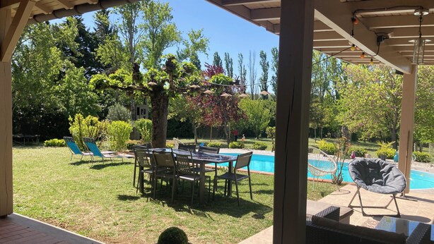 Uma área externa coberta com piscina, espreguiçadeiras e uma mesa sob uma pérgola.