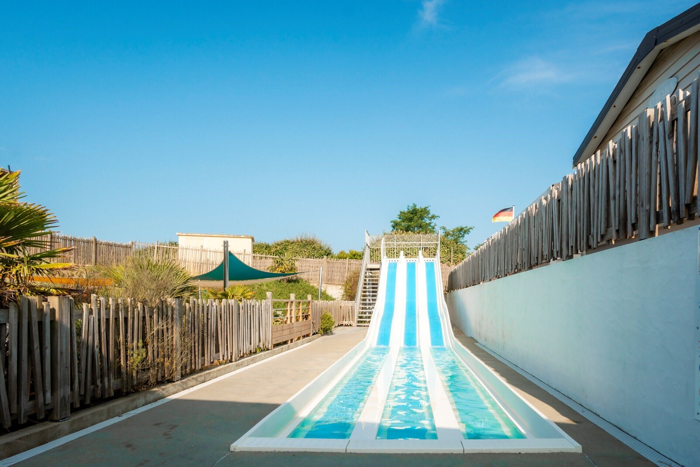 A water slide with a wooden fence on one side and a white wall on the other.