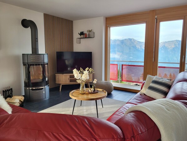 A living room with a fireplace, a TV, a sofa, and a balcony with a mountain view.