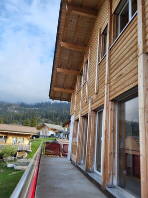 A wooden building with large windows and a balcony overlooking a mountainous area.