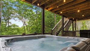 Ein Whirlpool in einem überdachten Außenbereich mit Holzterrasse, umgeben von Bäumen.