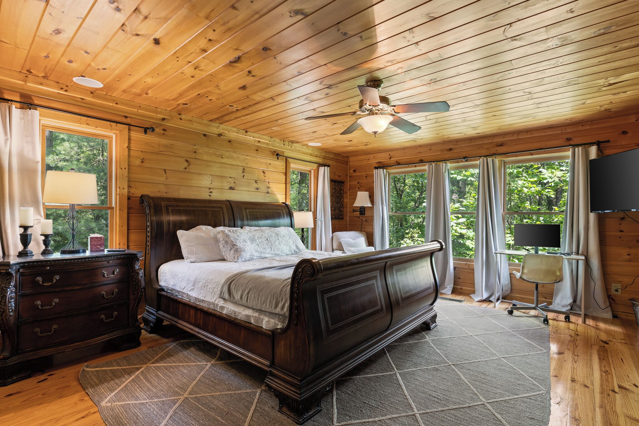 A wooden-paneled bedroom with a large bed, a desk, and a television.