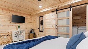 Ein Zimmer mit Holzwänden, einem Bett, einem an der Wand befestigten Fernseher, einer Schiebetür und einem kleinen Schrank mit einer Pflanze.