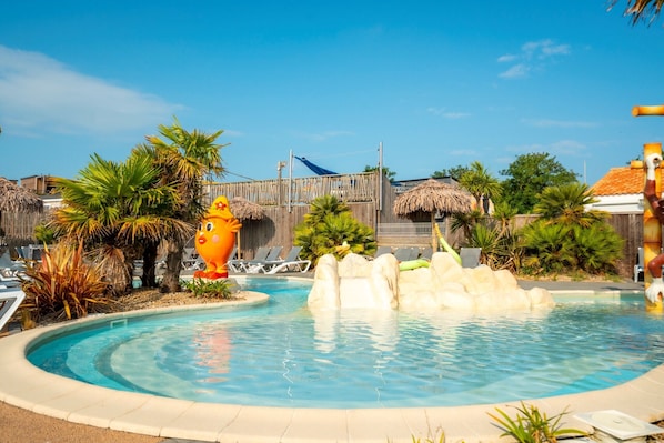 Ein Swimmingpool mit Felsformation, Liegestühlen, Palmen und strohgedeckten Hütten.