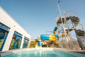 En swimmingpool med en vattenrutschkana, en byggnad med blåfärgade fönsterramar och en metalltrappa.