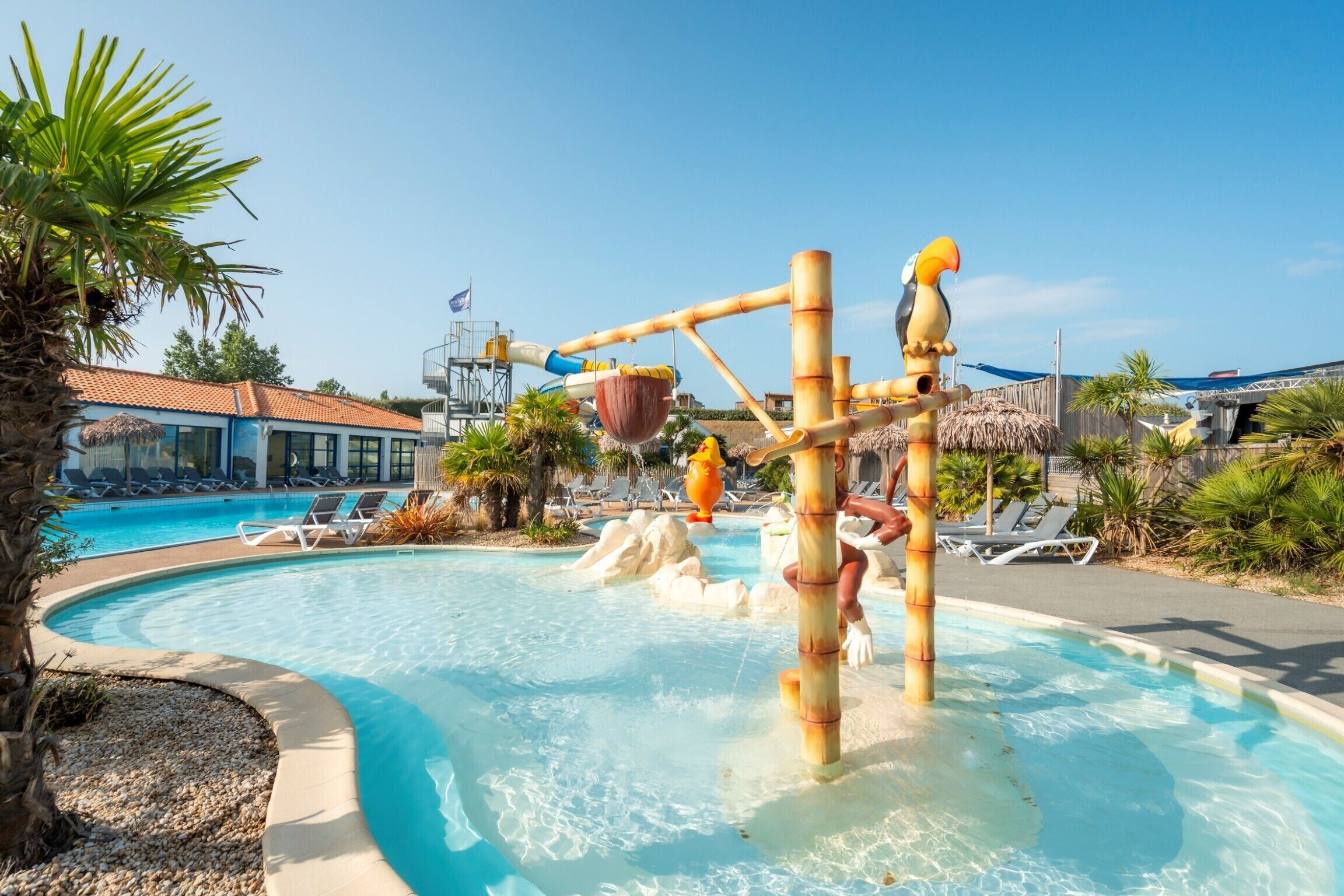 Una piscina con tobogán de agua, sillas de descanso y palmeras.