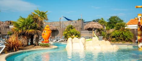 Ein Swimmingpool mit Felsformation, Liegestühlen, Palmen und strohgedeckten Hütten.