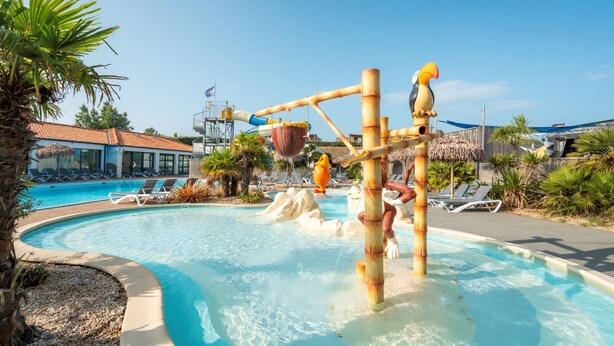 A swimming pool with a water slide, lounge chairs, and palm trees. - Carva - Confort 3 TV - 6p (3) (La Guérinière)