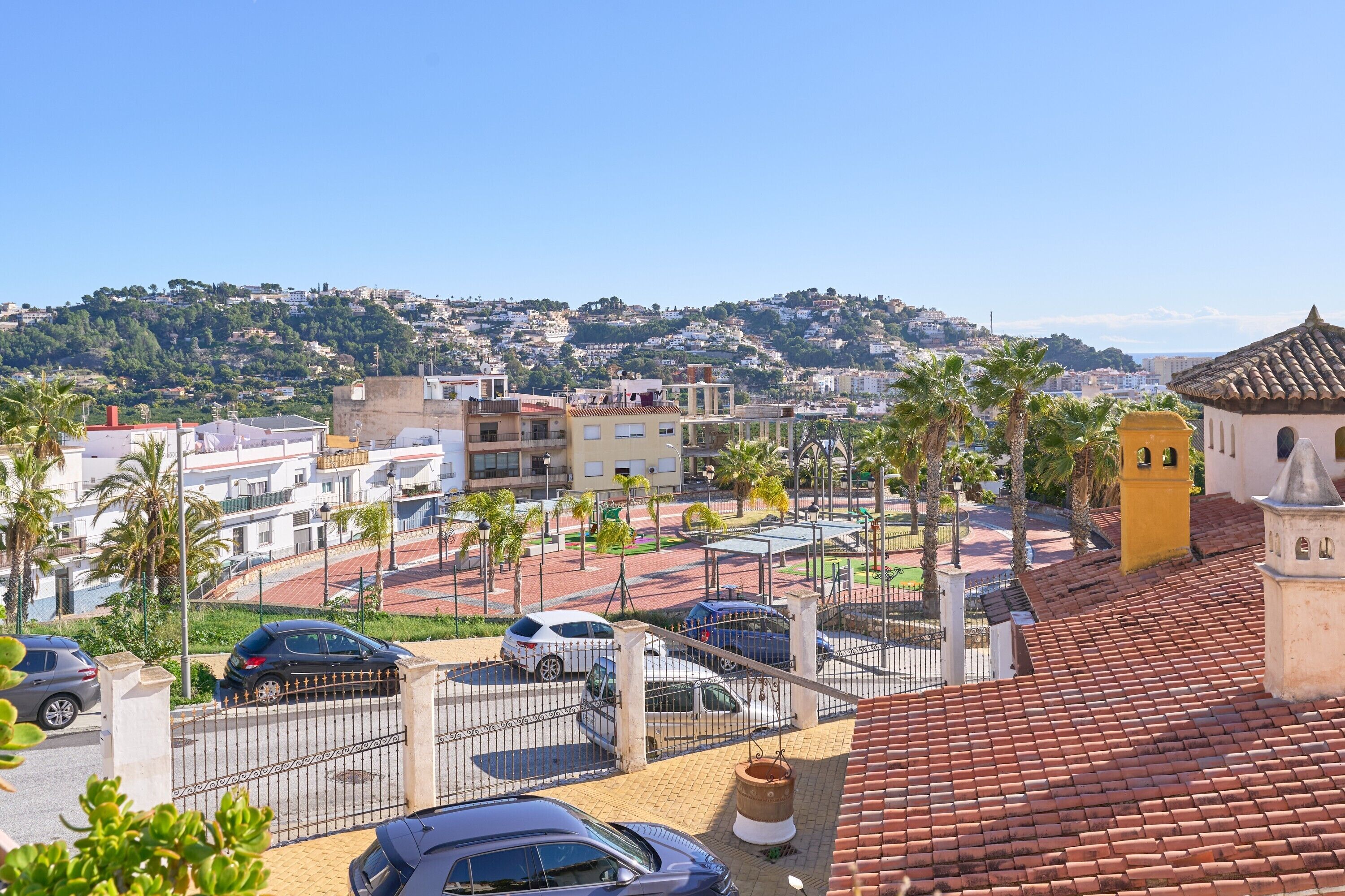 A residential area with a gated parking area, a church with a bell tower, and a hillside with houses.