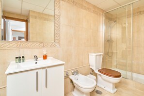 Een badkamer met een wastafel, toilet, douche en bidet.