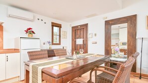 A dining area with a wooden table, wicker chairs, a refrigerator, and a window with blinds.