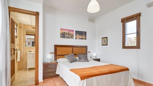 A bedroom with a bed, bedside tables, a nightstand, a window, and a bathroom visible through an open door.
