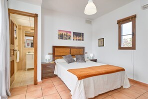 A bedroom with a bed, bedside tables, a nightstand, a window, and a bathroom visible through an open door.