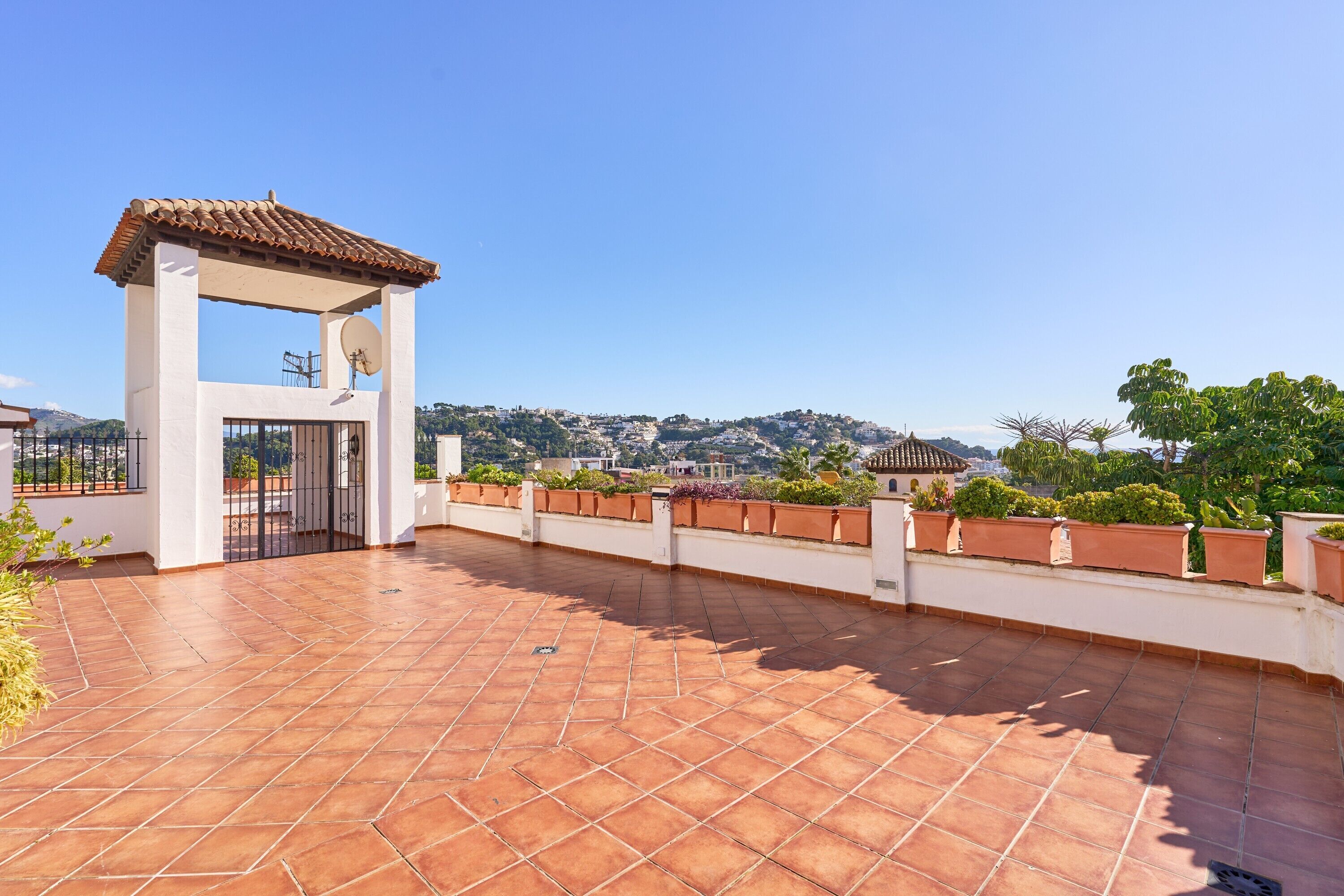 Una terraza en la azotea con tejas de terracota, una pérgola y vistas a un paisaje montañoso.