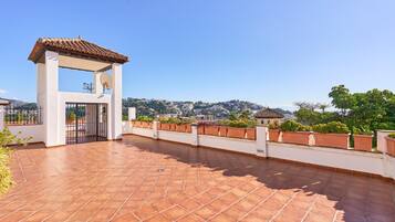 Una terraza en la azotea con tejas de terracota, una pérgola y vistas a un paisaje montañoso.