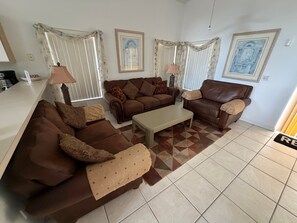 Ein Wohnzimmer mit zwei braunen Sofas, einem Couchtisch und gemusterten Vorhängen.