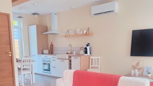 A modern living room with a sofa, a TV mounted on the wall, and a kitchen area in the background. - La Forge by L'Ora, a haven of peace 2 steps from the center of Cassel (Cassel)