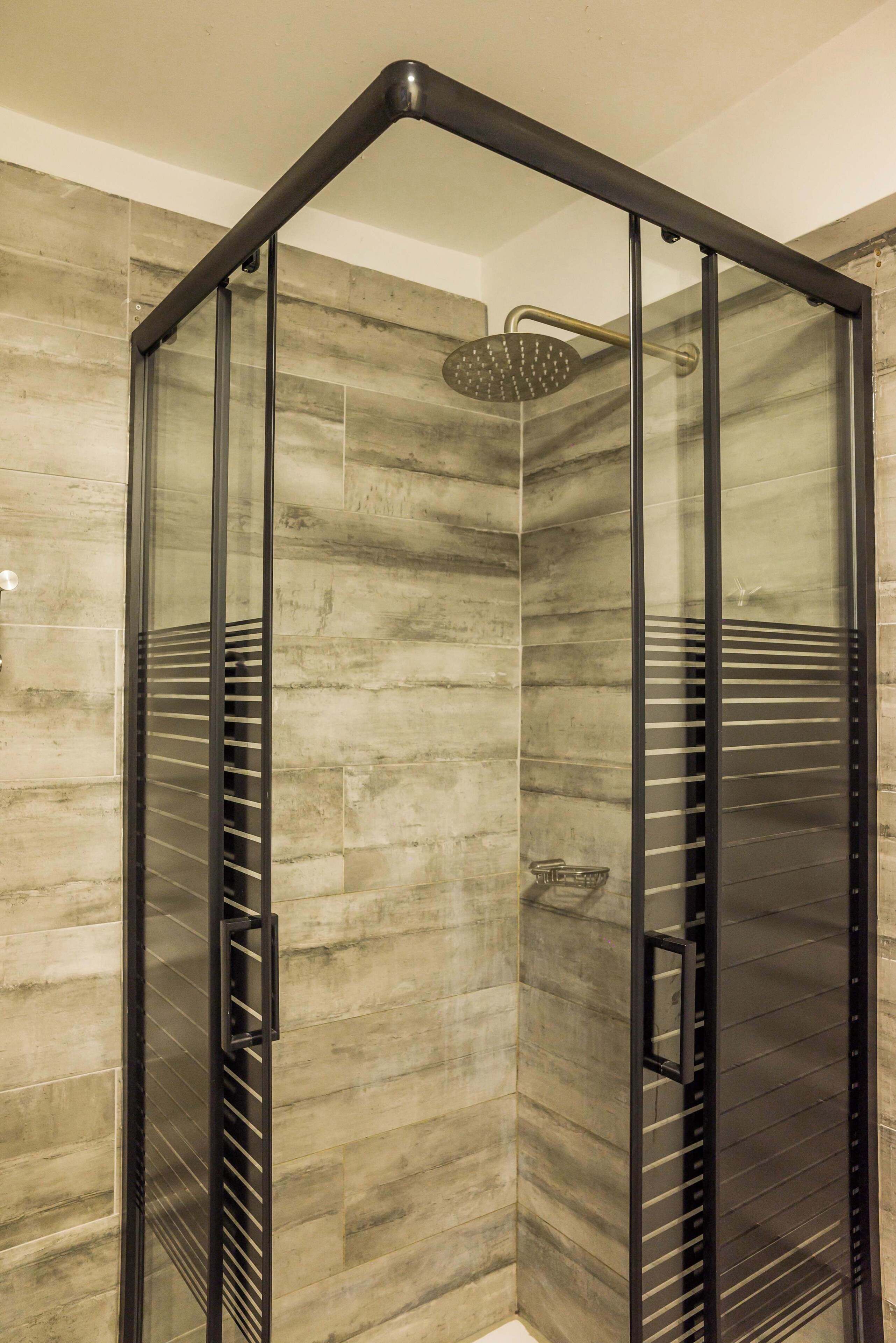 A glass-enclosed shower with a modern design, featuring a rain shower head and a built-in shelf.