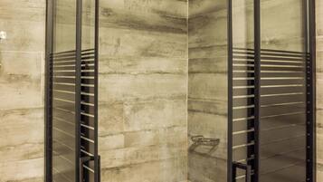 A glass-enclosed shower with a modern design, featuring a rain shower head and a built-in shelf.