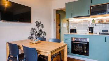 A modern kitchen with teal cabinets, a built-in oven, and a dining area with a wooden table and chairs.