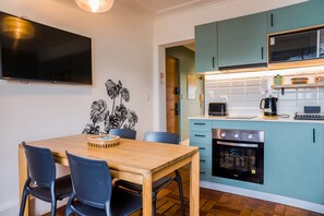 A modern kitchen with teal cabinets, a built-in oven, and a dining area with a wooden table and chairs. - Comfortable Apartment with Full Kitchen and Wifi (Providencia)