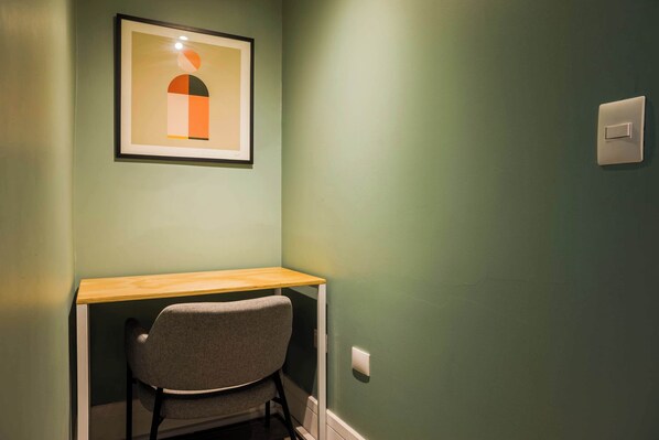 A room with a desk, chair, framed artwork, and a light switch on the wall.