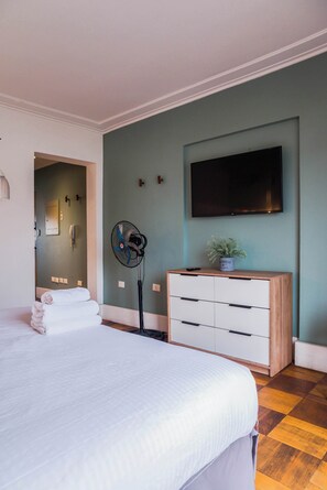 A bedroom with a bed, a dresser, a TV, a fan, and a plant.