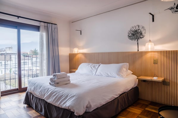 Habitación de hotel con cama, ventana grande, lámpara de pared y vista al exterior.