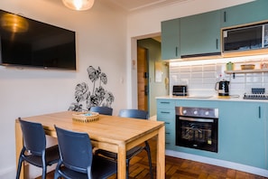 Una cocina moderna con armarios color turquesa, horno empotrado y comedor con mesa y sillas de madera.