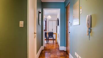 A hallway with a wooden floor, a dining area with chairs and a table, and a wall-mounted telephone.
