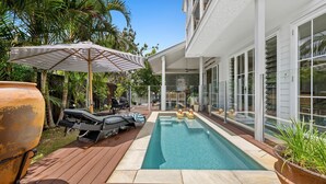 Un espace piscine extérieur moderne, doté d’une terrasse en bois, de chaises longues et d’un grand parasol.