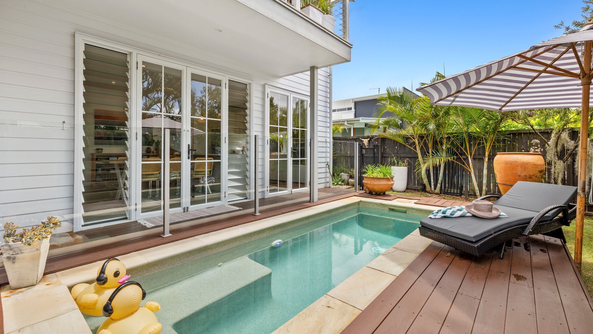 Ein Garten mit Pool, überdachter Terrasse und einer Holzterrasse.