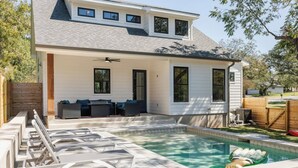 Una casa con piscina, mobiliario exterior y un patio cubierto.