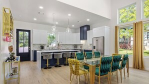 Una cocina moderna con armarios blancos, una isla central con taburetes de bar y una zona de comedor con sillas tapizadas en verde.