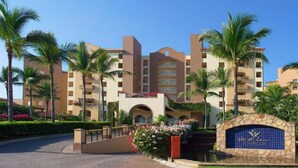 Un hotel con un patio central, palmeras y un letrero azul con el nombre del hotel.