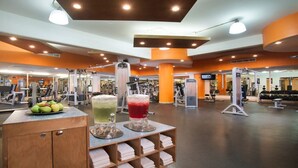Un gimnasio con equipos de ejercicio variados, una barra de jugos y un espejo.