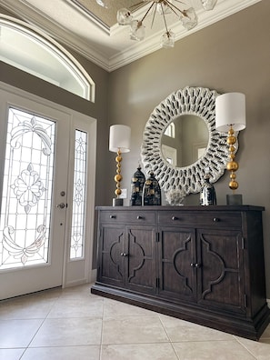 A dark wooden cabinet with a decorative mirror and two lamps, a door with stained glass, and a ceiling with a chandelier.