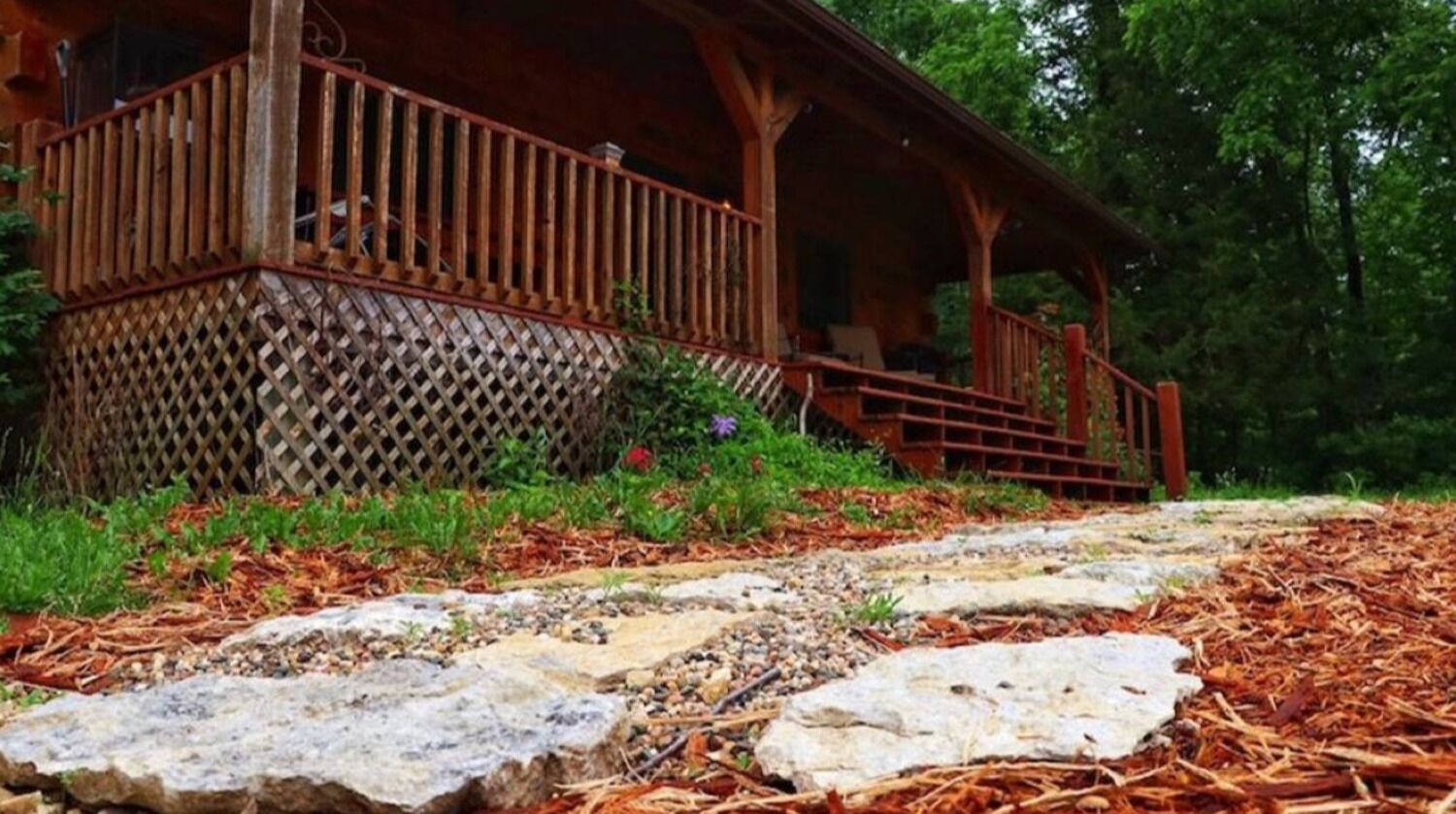 Une cabane en bois dotée d’un porche couvert et d’un escalier en pierre menant à une terrasse en bois.