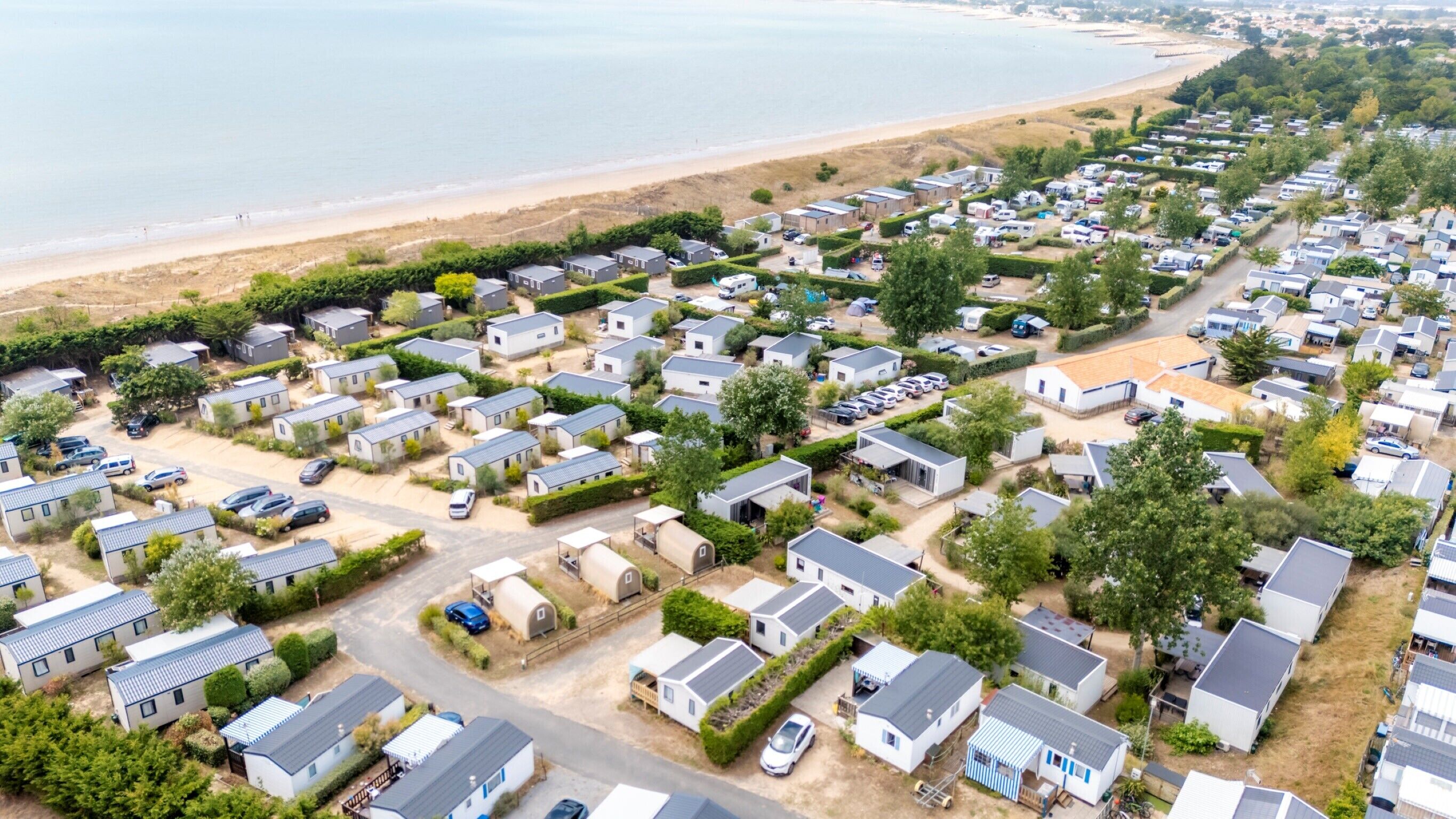 A large caravan park with numerous mobile homes, a beach in the background, and a clear sky.