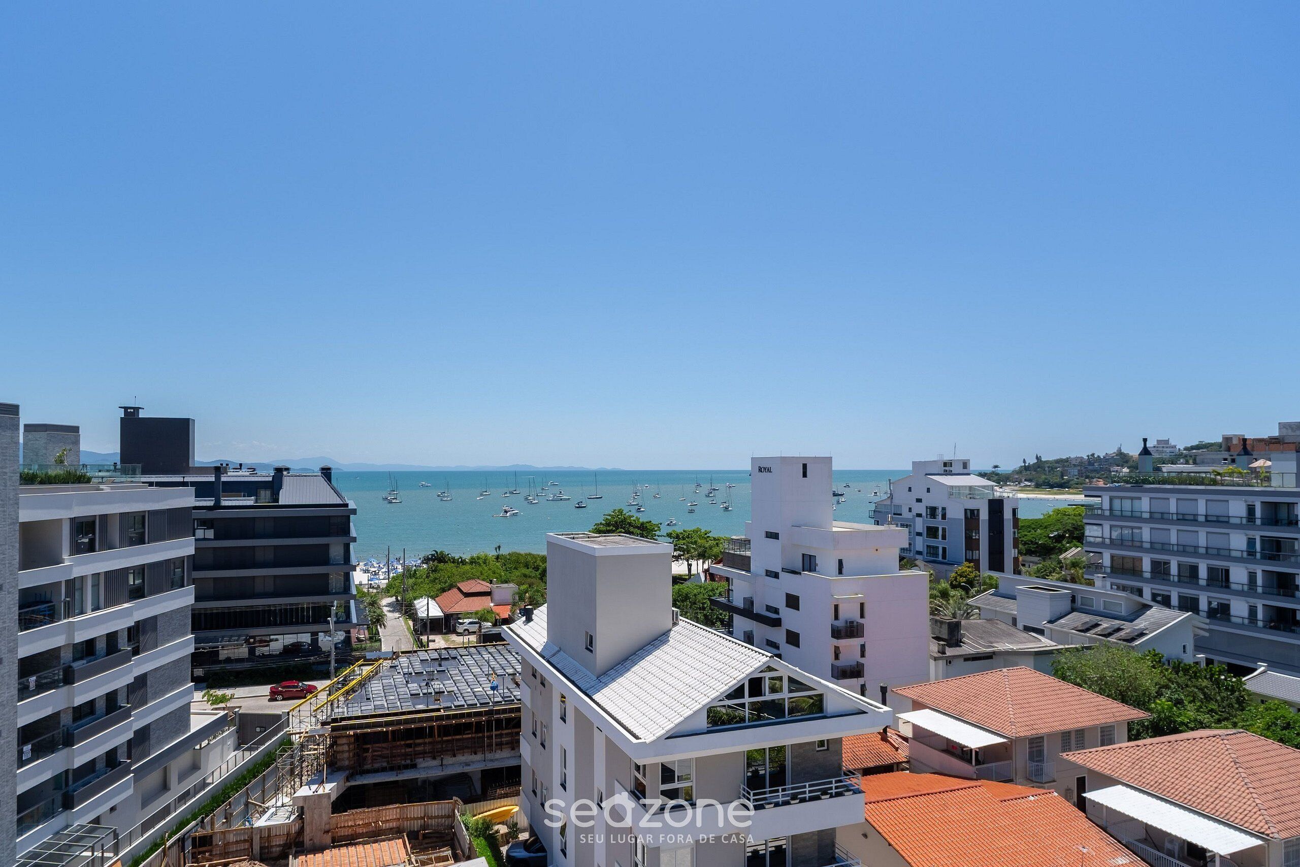 A coastal cityscape with modern buildings, a marina with boats, and clear skies.