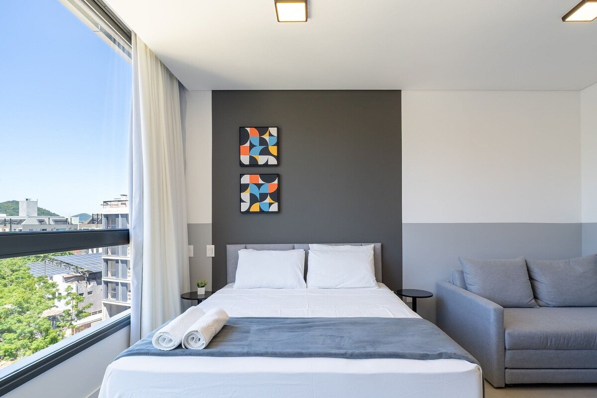 A modern hotel room with a large bed, a grey sofa, and two abstract paintings on the wall.