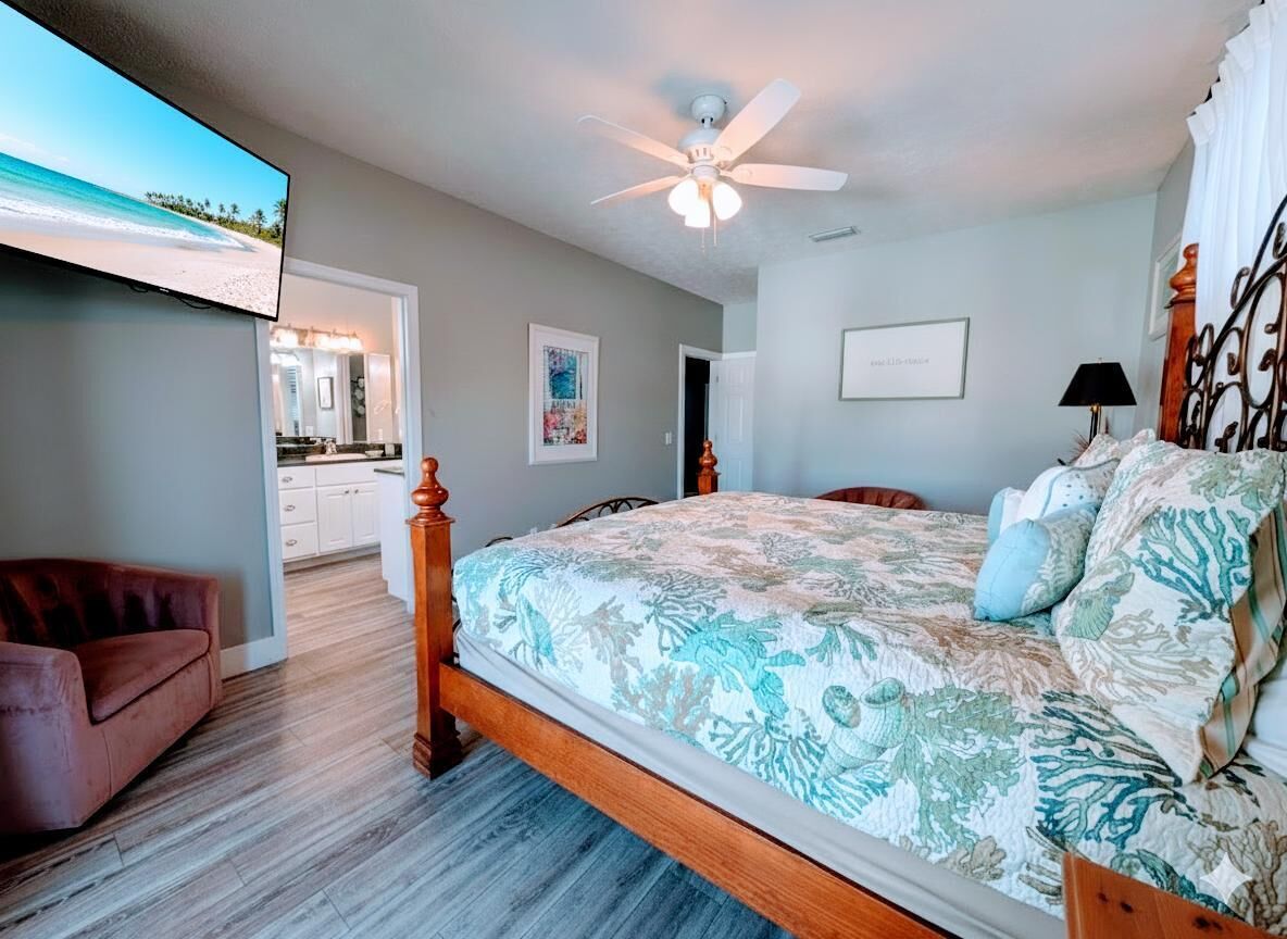 Un dormitorio con cama, ventilador de techo, televisión y vista al mar.