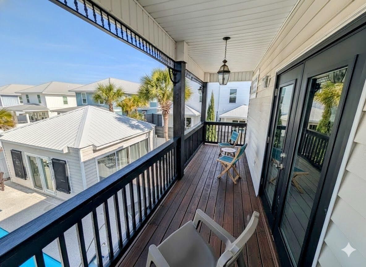 A balcony with a view of neighboring houses, a wooden deck, and a hanging light fixture.